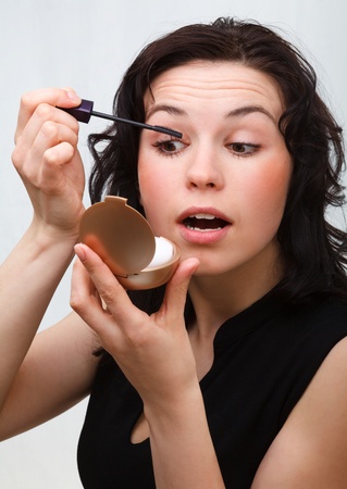 Young woman is applying mascara while looking at herself in mirrorの写真素材