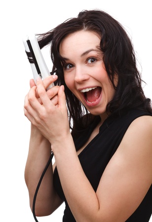 Young woman is screaming while using hair straightener, isolated over whiteの写真素材