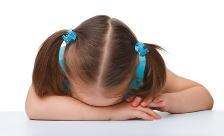 Little girl is sleeping at table laying her head on hands, isolated over whiteの写真素材
