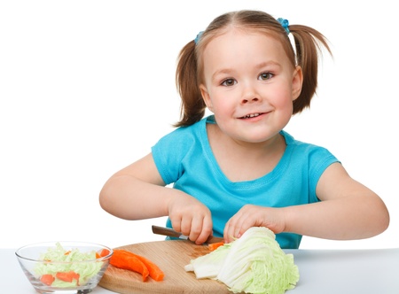 Little girl is cutting carrot for salad using kitchen knife, isolated over whiteの写真素材