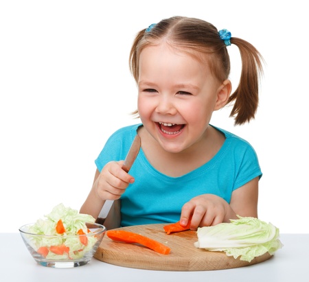 Little girl is cutting carrot for salad using kitchen knife, isolated over whiteの写真素材