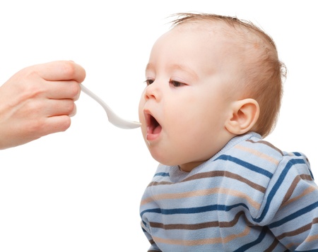 Cute little boy is being fed using spoon, isolated over whiteの写真素材