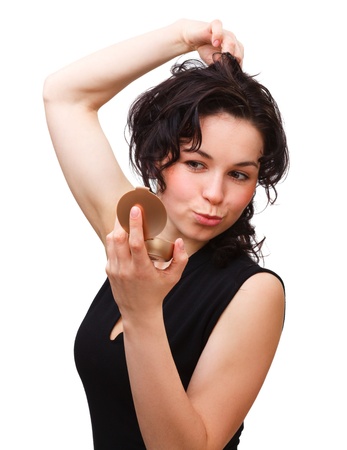 Young attractive girl is looking at herself in mirror while holding her hair up, isolated over whiteの写真素材
