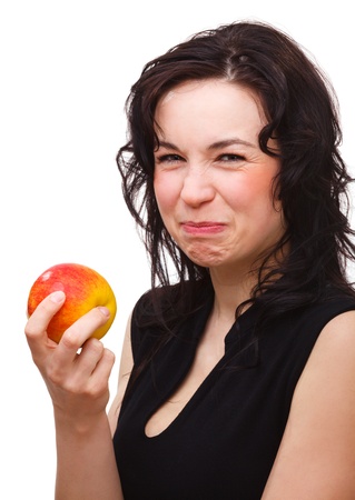 Young attractive woman is making sour face after biting red apple, isolated over whiteの写真素材