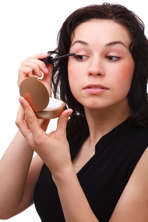 Young woman is applying mascara while looking at herself in mirror, isolated over whiteの写真素材