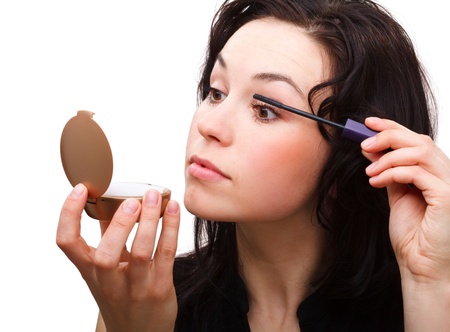 Young woman is applying mascara while looking at herself in mirror, isolated over whiteの写真素材