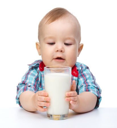 Cute little boy is holding big glass of milk while sitting at table, isolated over whiteの写真素材