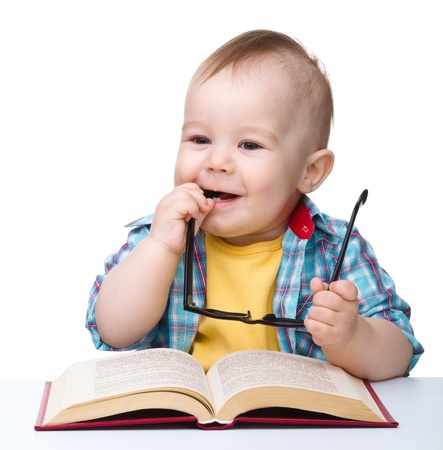 Cute little child play with book and glasses while sitting at table, isolated over whiteの写真素材