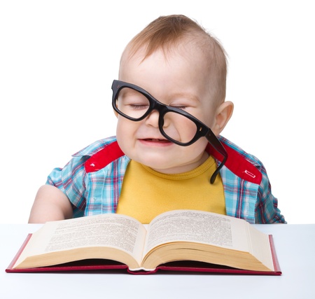 Cute little child play with book and glasses while sitting at table, isolated over whiteの写真素材
