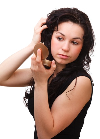Young attractive girl is looking at herself in mirror while holding her hair up, isolated over whiteの写真素材