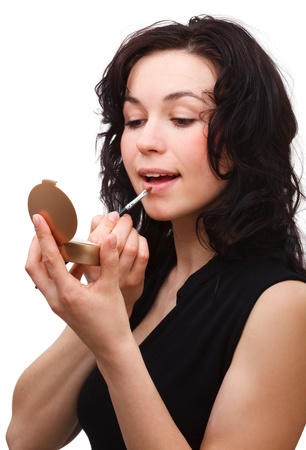 Young woman is applying lipgloss using brush while looking at herself in mirror, isolated over whiteの写真素材