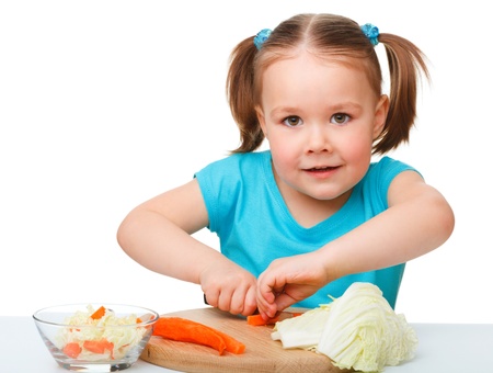 Little girl is cutting carrot for salad using kitchen knife, isolated over whiteの写真素材