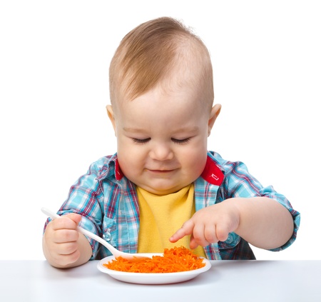 Cute little boy is playing with carrot salad, isolated over whiteの写真素材
