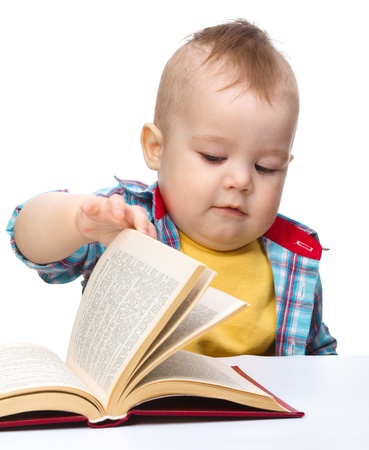 Cute little child play with book while sitting at table, isolated over whiteの写真素材