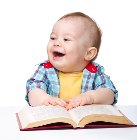 Cute little child play with book while sitting at table, isolated over whiteの写真素材