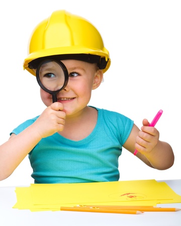 Cute little girl is looking through magnifier wearing hard hat, isolated over whiteの写真素材