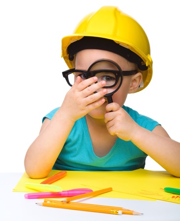 Cute little girl is looking through magnifier wearing hard hat, isolated over whiteの写真素材