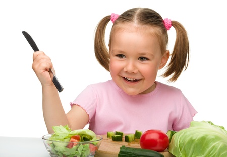 Little girl is cutting carrot for salad using kitchen knife, isolated over whiteの写真素材