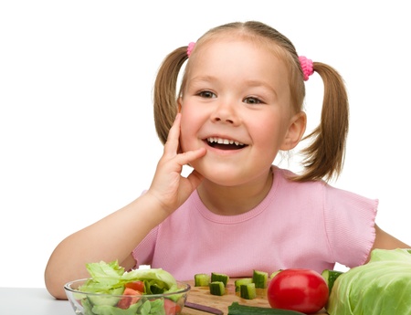 Little girl is cutting carrot for salad using kitchen knife, isolated over whiteの写真素材