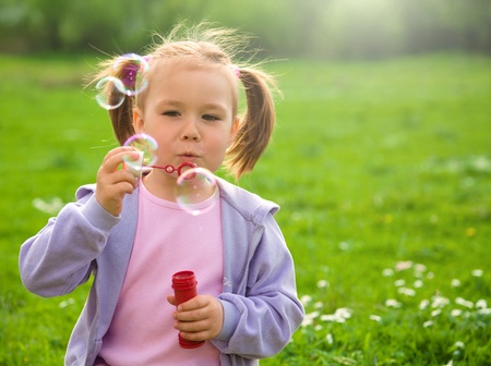 Little girl blows soap bubbles on green meadowの写真素材