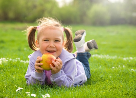 Little girl is laying on green meadow and going to eat a red appleの写真素材