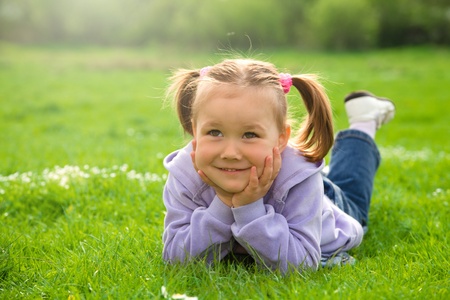 Little girl is laying on green meadow holding her head with handsの写真素材