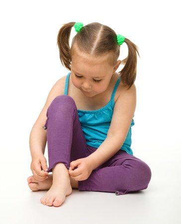 Portrait of a cute little girl sitting on floor straightening her trousers, isolated over whiteの写真素材