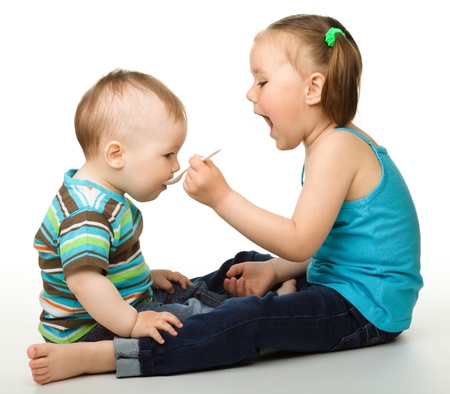 Sister is feeding her little brother using spoon, isolated over whiteの写真素材