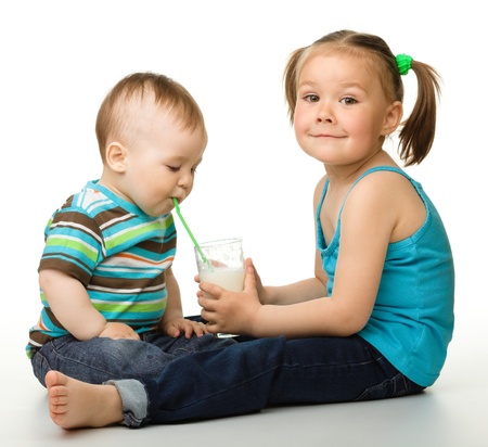 Sister is feeding her little brother and he drinks milk using drinking straw, isolated over whiteの写真素材