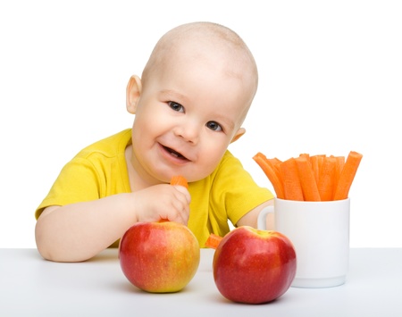 Cute little boy eats carrot and apples, isolated over whiteの写真素材