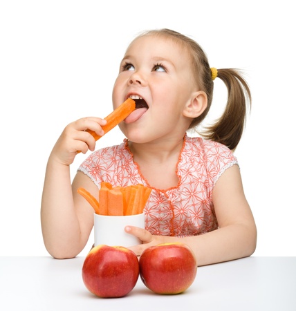 Cute little girl eats carrot and apples, isolated over whiteの写真素材