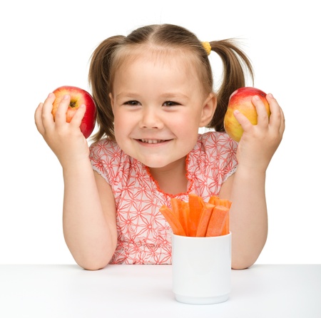 Cute little girl eats carrot and apples, isolated over whiteの写真素材