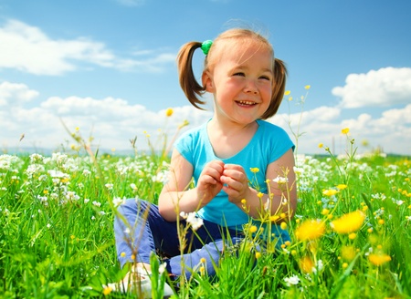 Little girl is playing while sitting on green meadowの写真素材