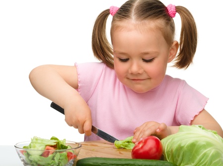 Little girl is cutting carrot for salad using kitchen knife, isolated over whiteの写真素材