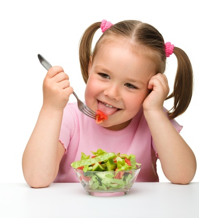Cute little girl eats vegetable salad using fork, isolated over whiteの写真素材