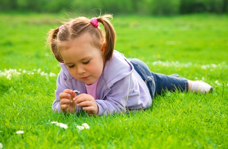 Little girl is laying on green meadow and smell daisyの写真素材