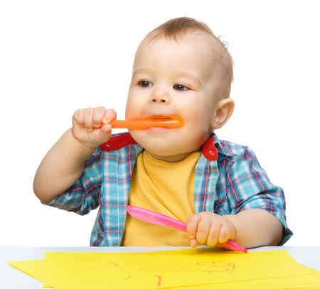 Happy little boy is playing with colorful markers, isolated over whiteの写真素材