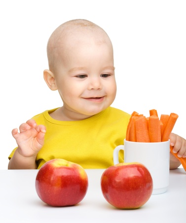 Cute little boy eats carrot and apples, isolated over whiteの写真素材
