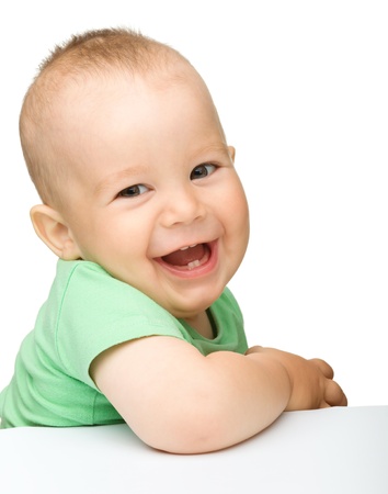 Portrait of a cute cheerful little boy, who is smiling while sitting at table, isolated over whiteの写真素材