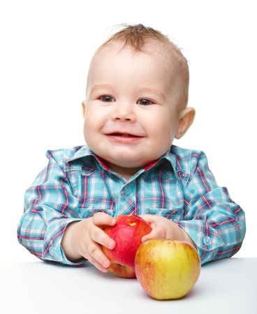 Cute little child is eating red apple while sitting at table, isolated over whiteの写真素材