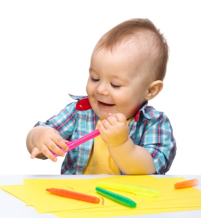 Happy little boy is playing with colorful markers, isolated over whiteの写真素材