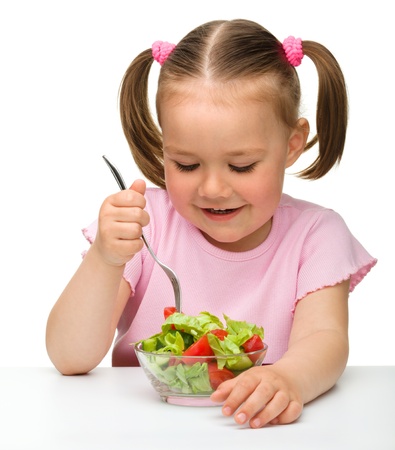 Cute little girl eats vegetable salad using fork, isolated over whiteの写真素材