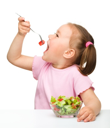 Cute little girl eats vegetable salad using fork, isolated over whiteの写真素材