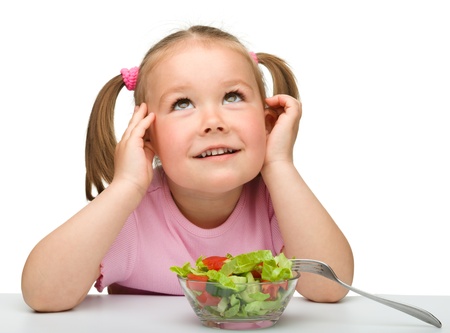 Cute little girl eats vegetable salad using fork, isolated over whiteの写真素材