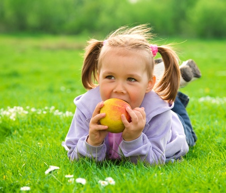 Little girl is laying on green meadow and going to eat a red appleの写真素材