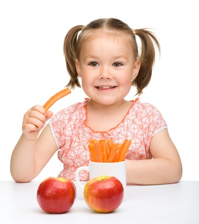 Cute little girl eats carrot and apples, isolated over whiteの写真素材