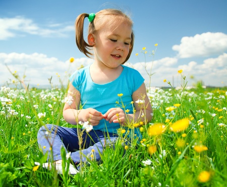 Little girl is playing while sitting on green meadowの写真素材