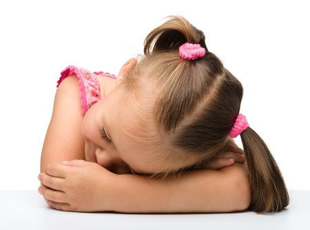 Little girl is sleeping at table laying her head on hands, isolated over whiteの写真素材
