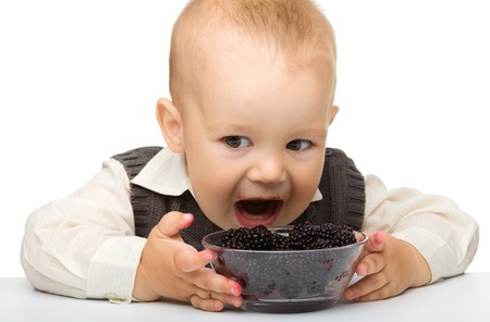 Cute little boy is eating blackberry, isolated over whiteの写真素材
