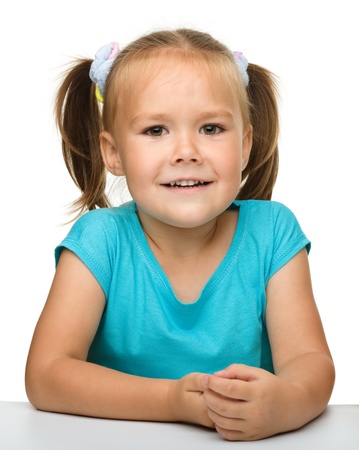 Happy little girl is sitting at the table, isolated over whiteの写真素材